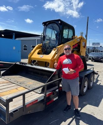 Customer beside a CAT skid steer loader on a trailer at IronPower Industries